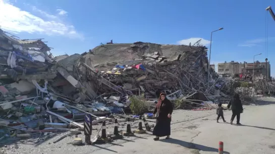 Een vrouw wandelt door een straat met verwoeste gebouwen in Turkije. De gevolgen van de aardbeving zijn rampzalig. - © Caritas Turkije